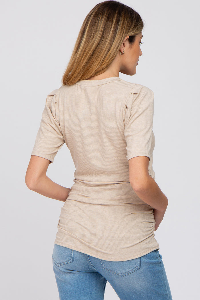 woman wearing a beige short sleeve maternity top with ruffle details on the shoulders and fitted silhouette