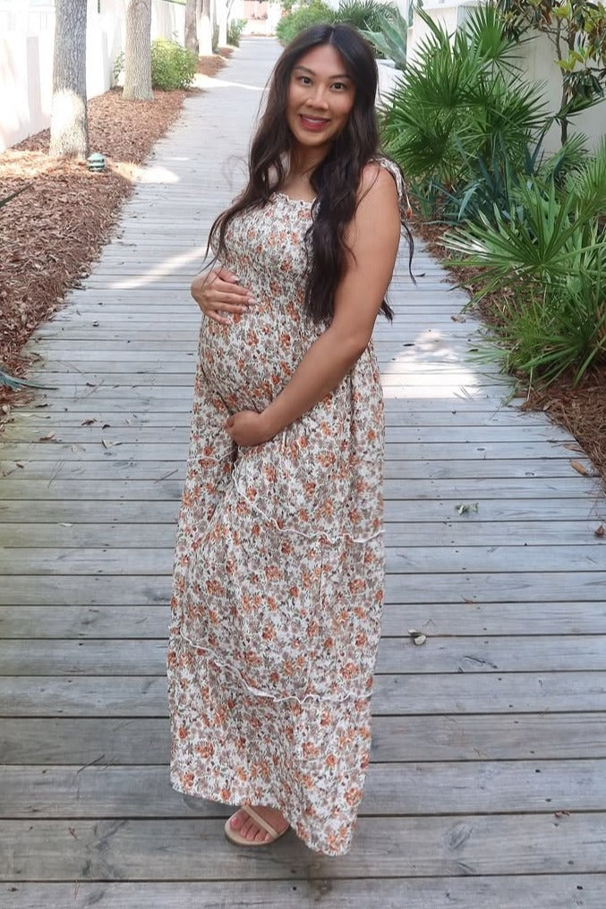 woman wearing a floral print maternity maxi dress and holding her baby bump while walking on a wooden pathway