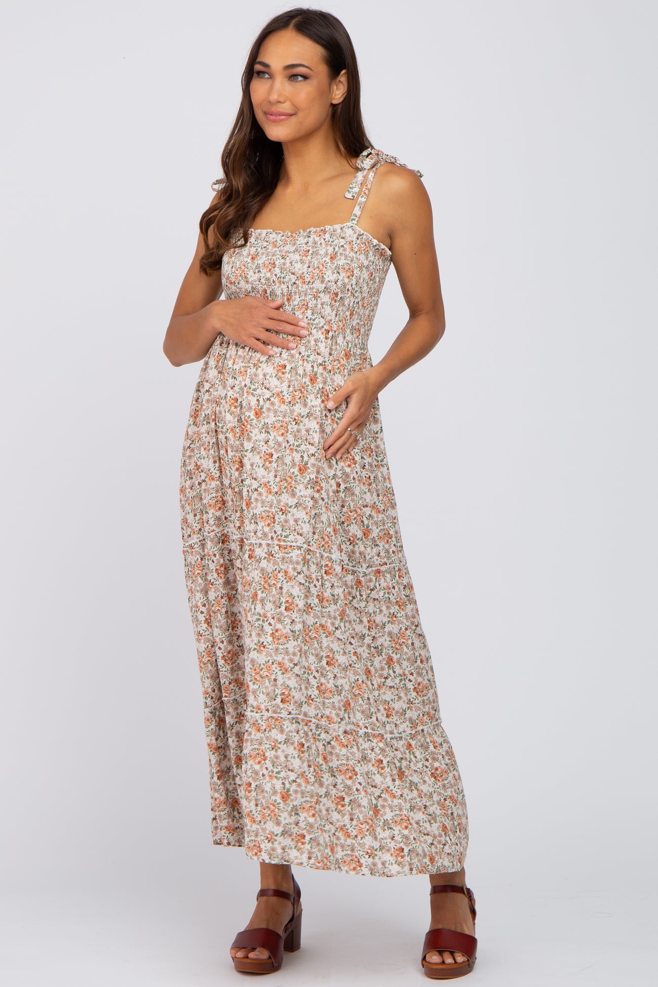 woman wearing a floral print maternity maxi dress with a smocked bodice and holding her baby bump