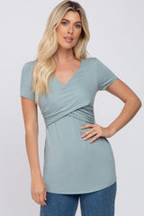 woman wearing a sage green short sleeve surplice maternity top with crossover front detail