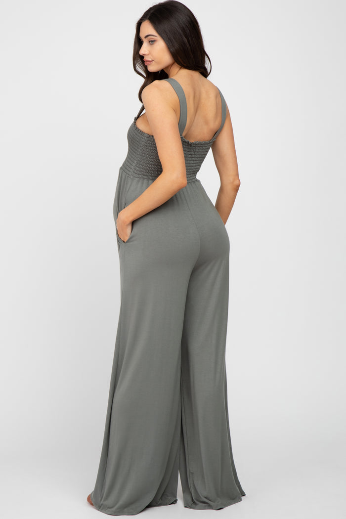 woman wearing a dark green maternity jumpsuit with smocked bodice and wide-leg pants, viewed from the back
