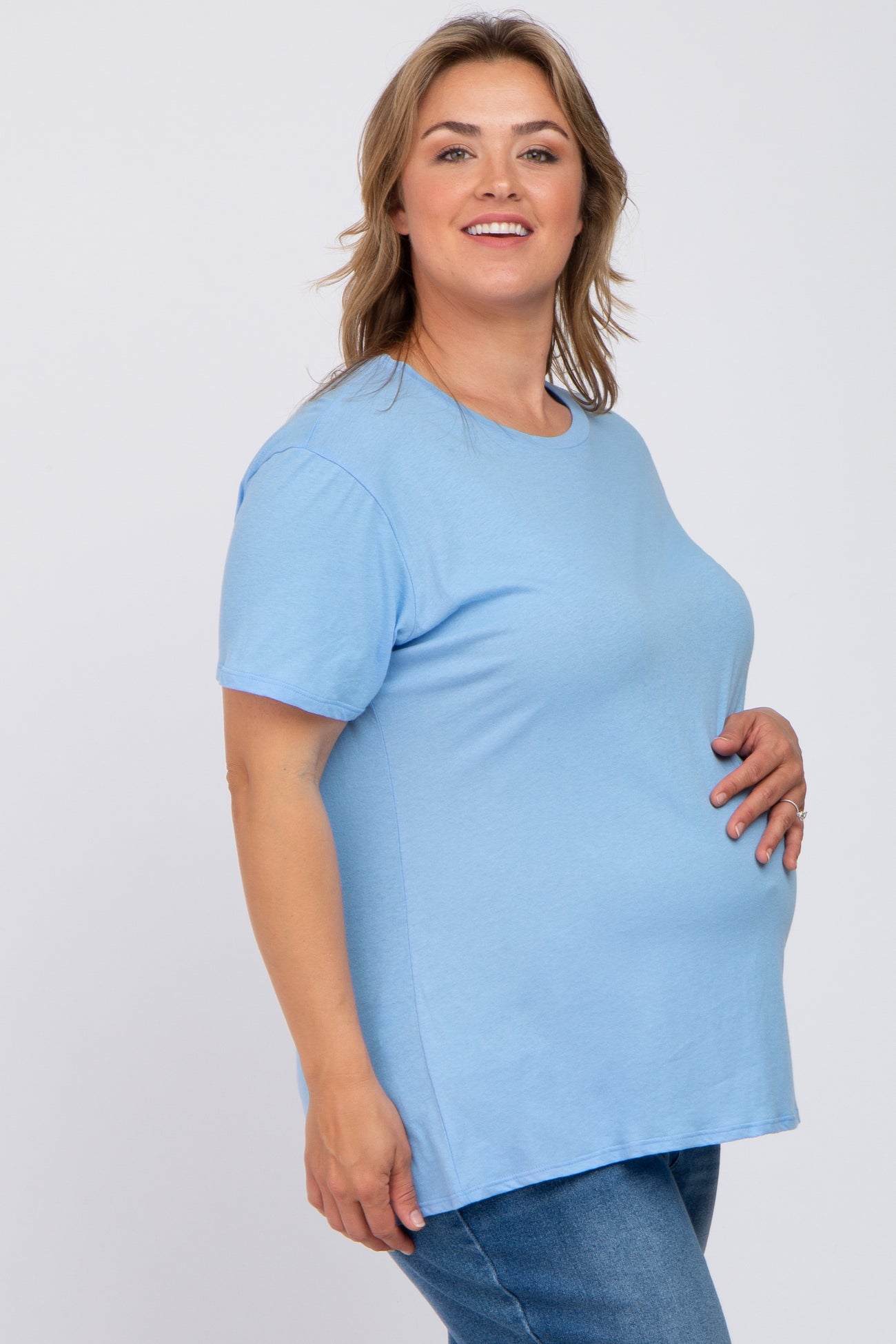 woman wearing a light blue short sleeve maternity top and holding her baby bump