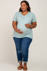 Pregnant woman in light blue v-neck maternity t-shirt and jeans holding her baby bump