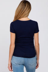 woman wearing a navy blue short sleeve maternity top with gathered details at the back and paired with light blue jeans