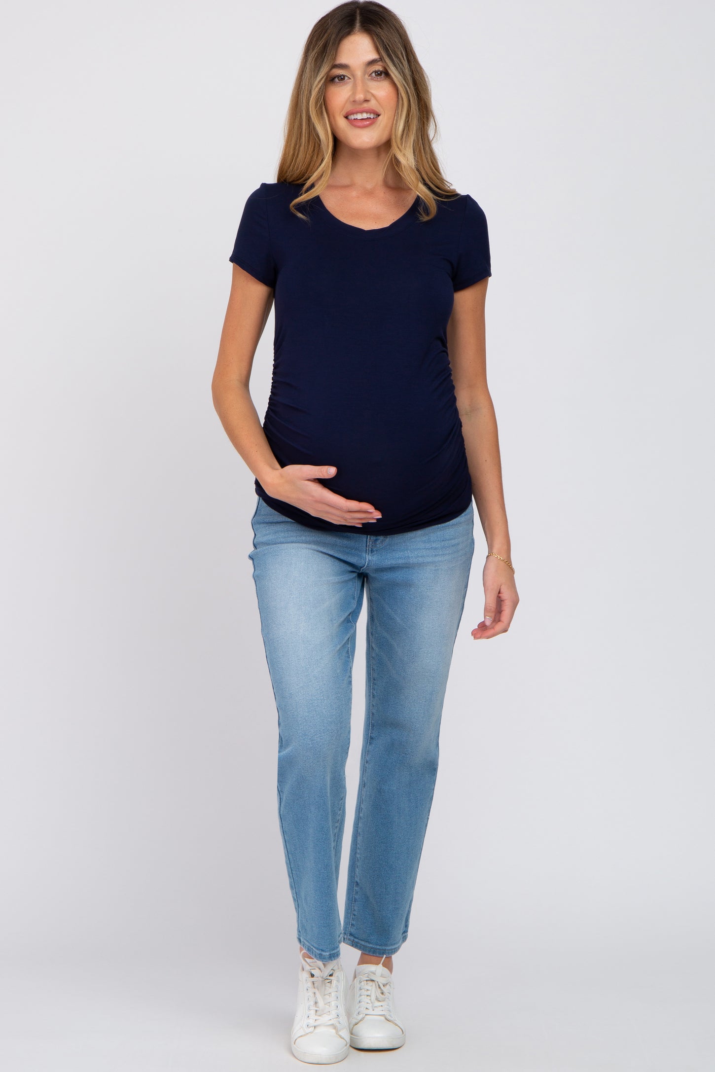 woman wearing a navy blue short sleeve maternity top and light blue jeans, gently cradling her baby bump