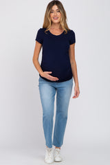 woman wearing a navy blue short sleeve maternity top and light blue jeans, gently cradling her baby bump