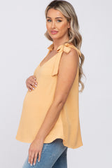 woman wearing a light orange maternity top with tie straps and a visible baby bump