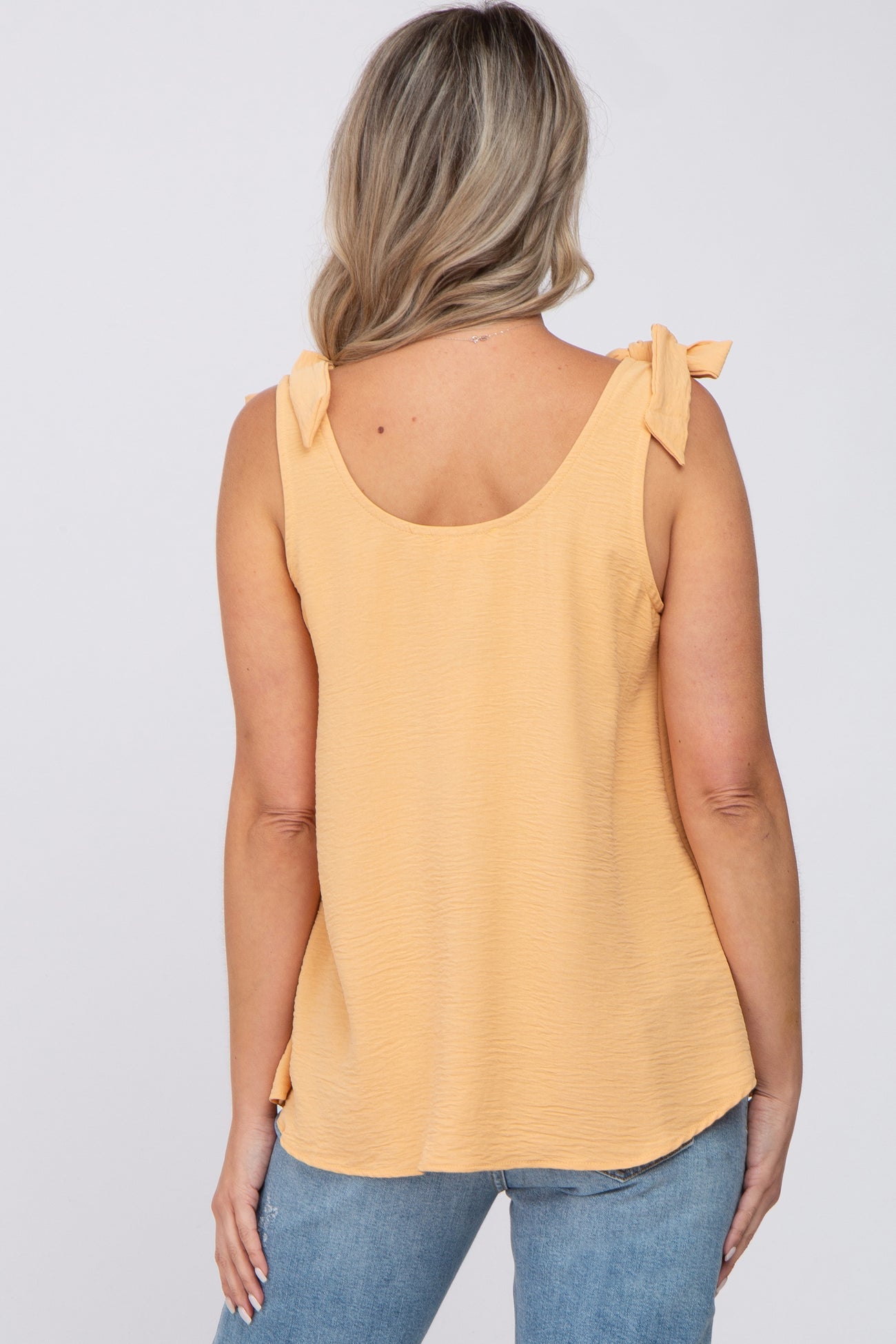 woman wearing a light yellow maternity top with tie shoulder details and a relaxed fit, viewed from the back