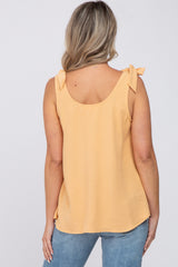 woman wearing a light yellow maternity top with tie shoulder details and a relaxed fit, viewed from the back