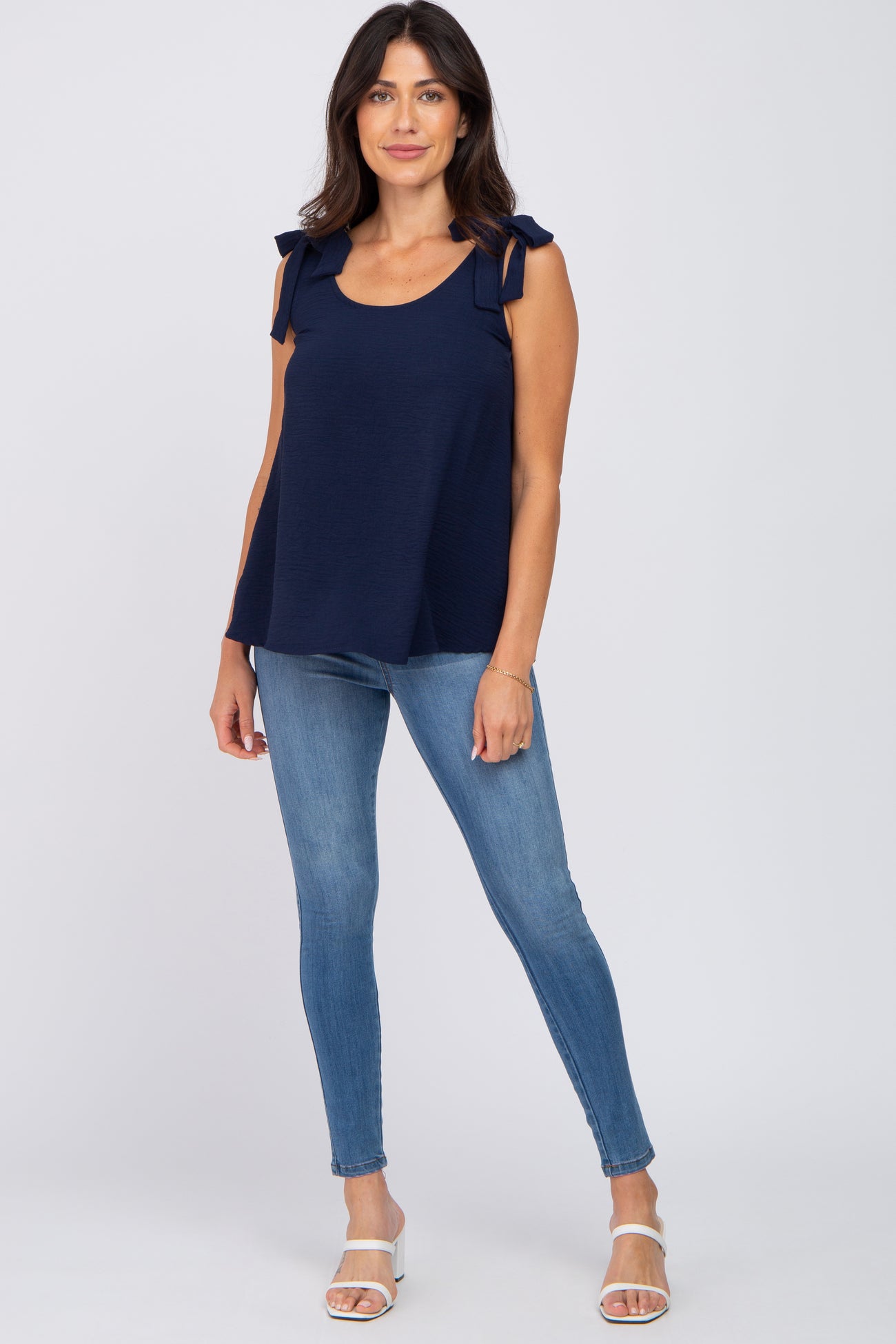 woman wearing a navy blue sleeveless top with tie shoulder details and light blue skinny jeans