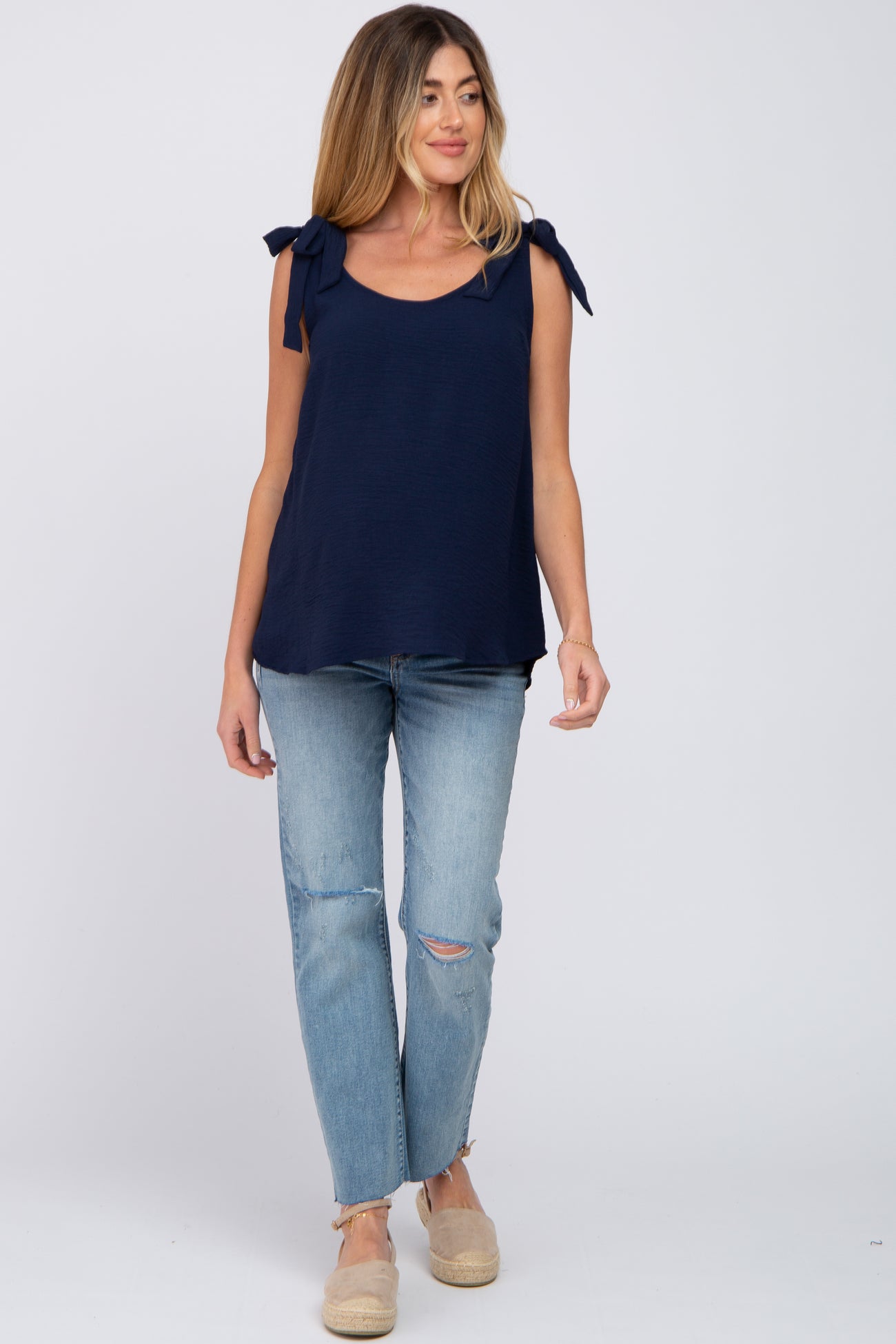 woman wearing a navy maternity top with tie shoulder details and paired with ripped light blue jeans