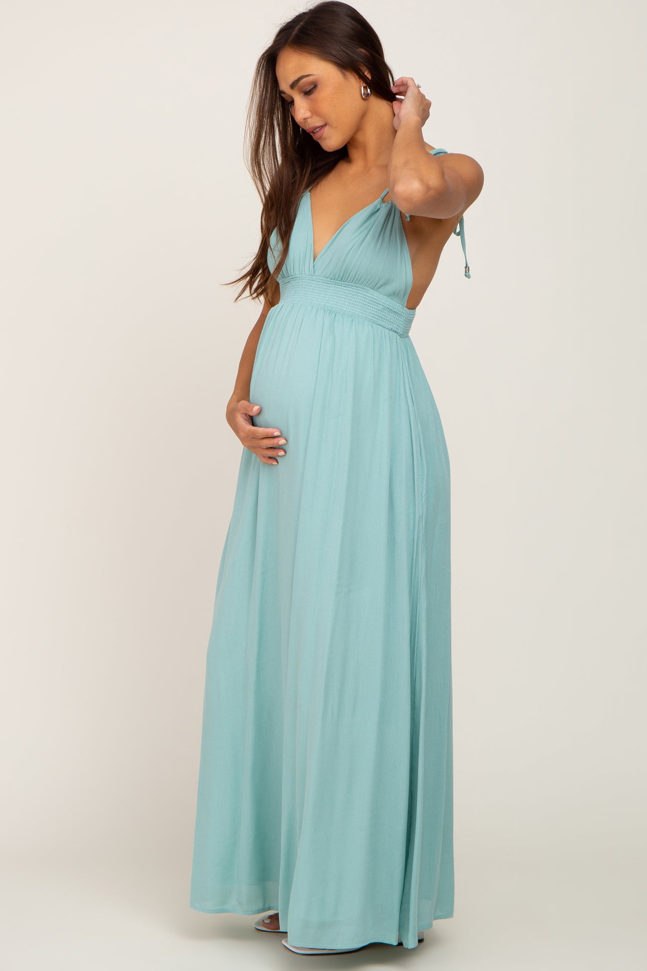 Pregnant woman wearing a light blue sleeveless maternity maxi dress with a smocked waist and V-neckline
