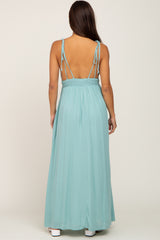 woman wearing a mint green backless maternity maxi dress with adjustable tie straps and a fitted waistband