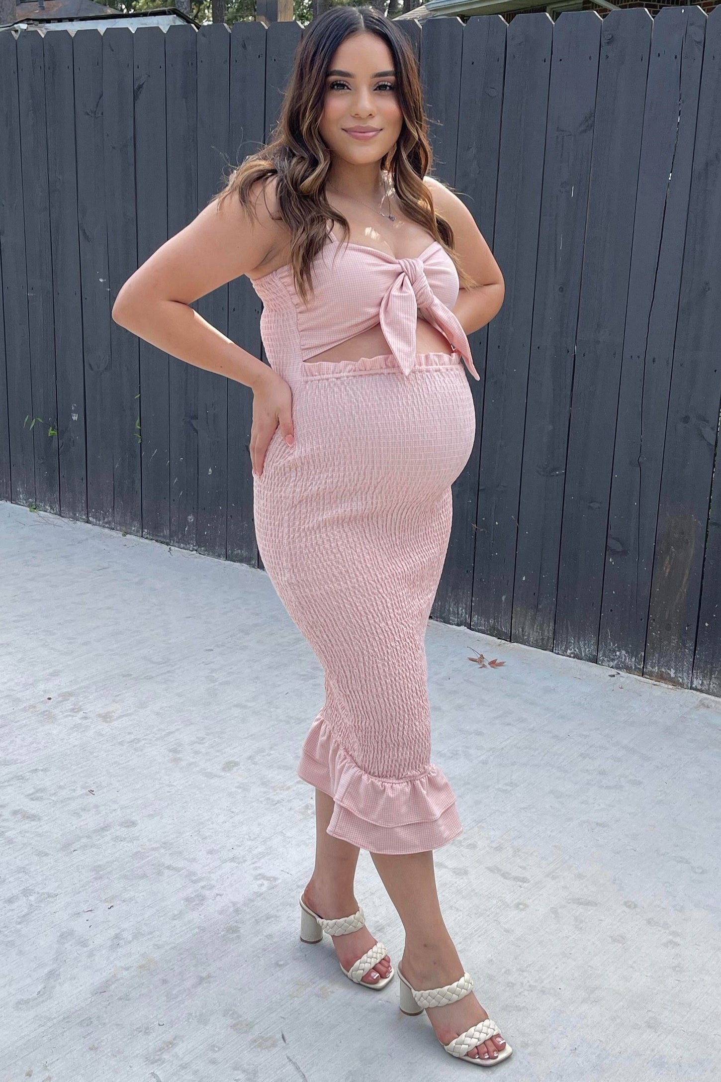woman wearing a pink maternity dress with a tie front and ruffled hem, showcasing her baby bump