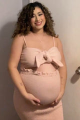 woman wearing a light pink maternity dress with a bow detail, showing her baby bump while smiling