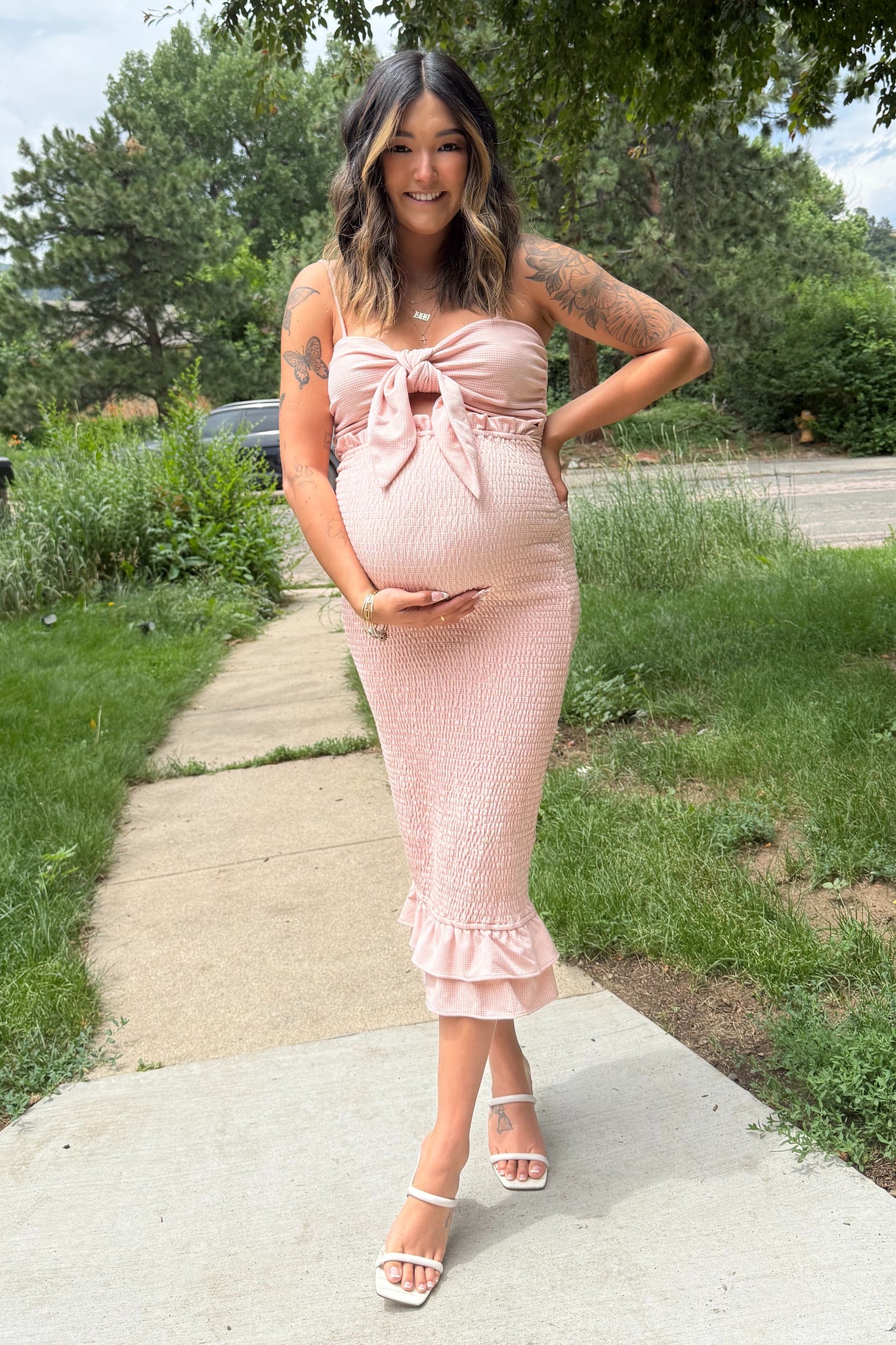 woman wearing a blush pink strapless maternity dress with a tie front and ruffled hem, showing her baby bump