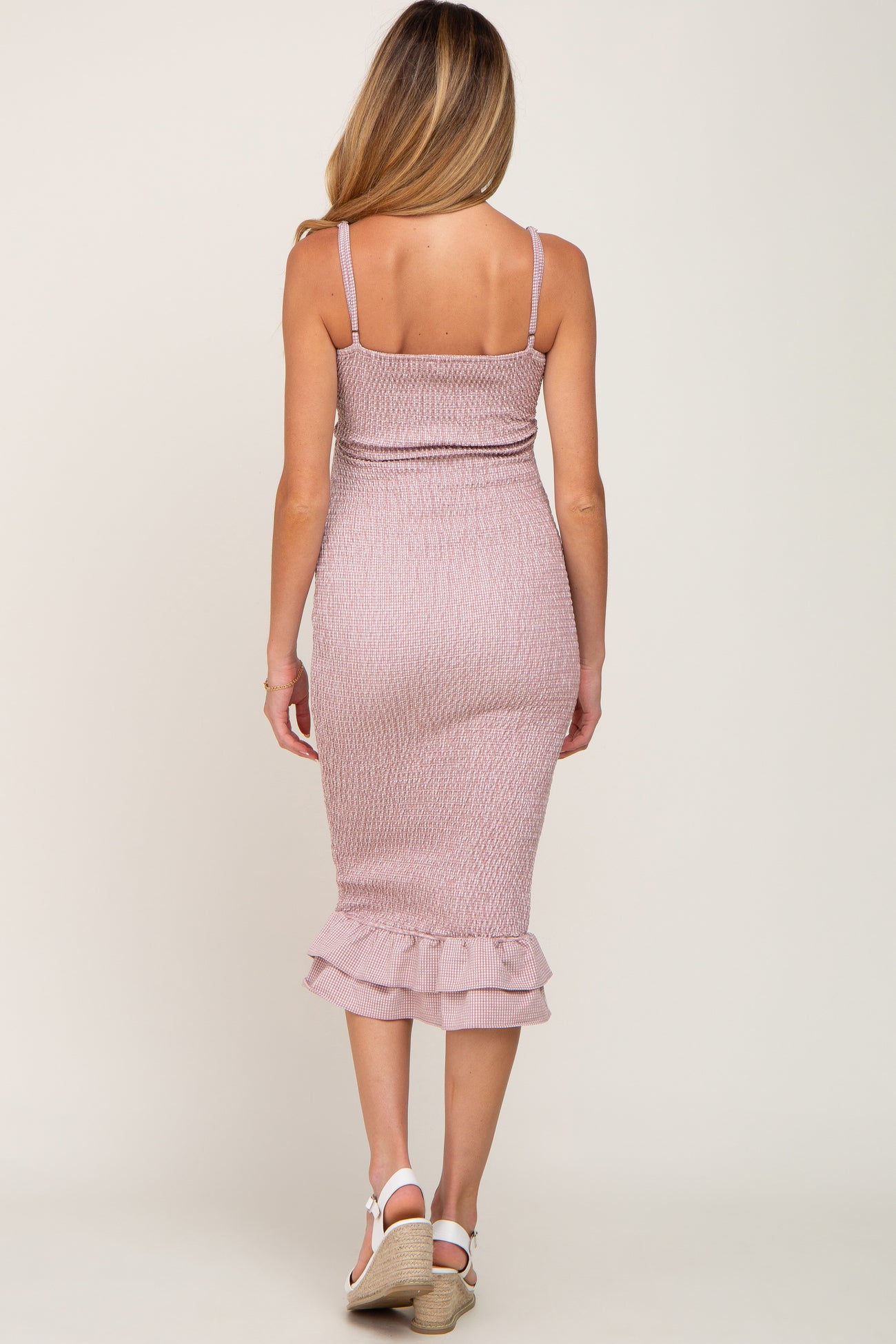 woman wearing a light pink maternity dress with smocked bodice and ruffle hem, showing off a baby bump from the back