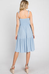 woman wearing a light blue smocked midi dress with adjustable straps and tiered skirt, viewed from the back
