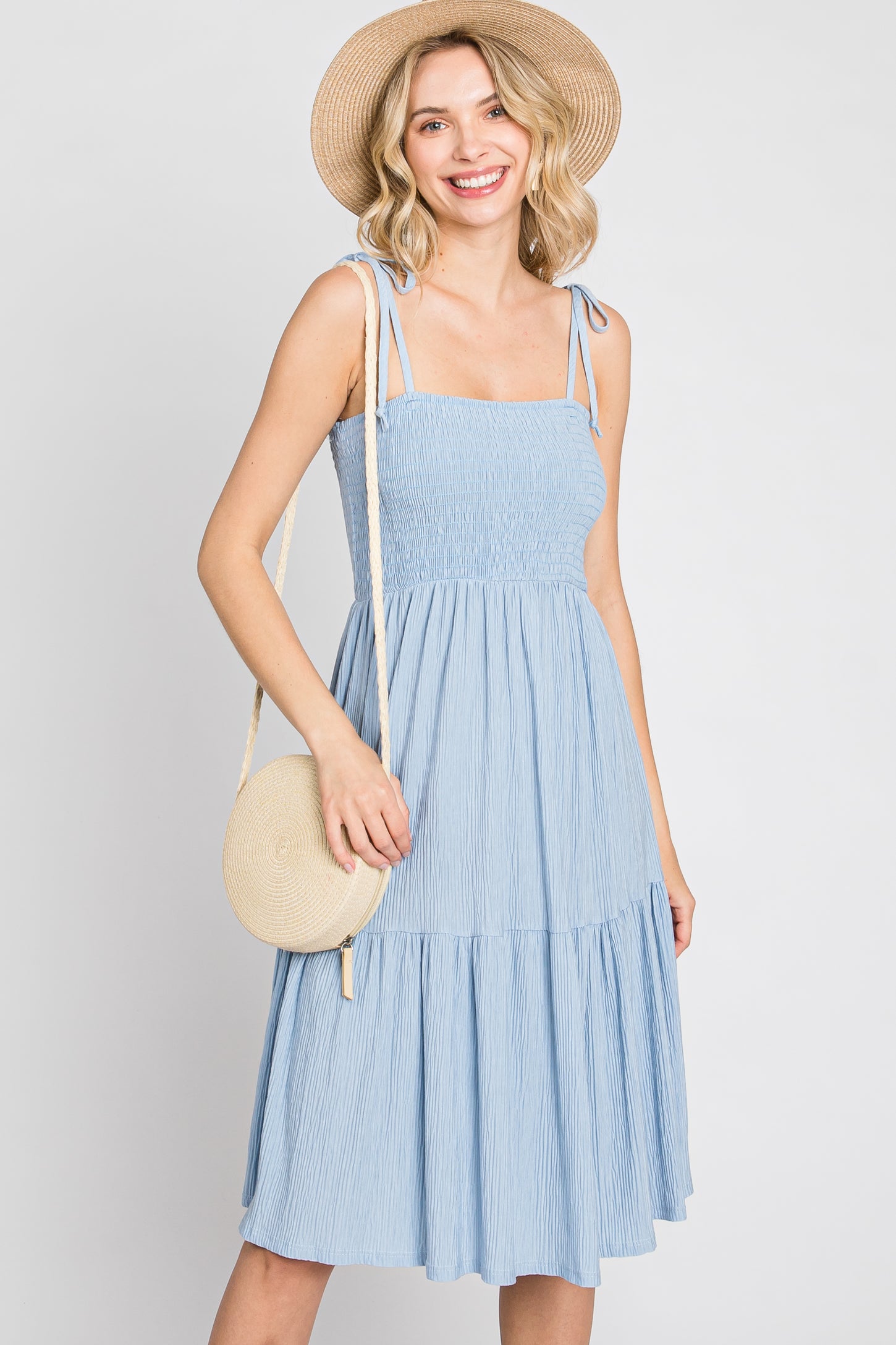 woman wearing a light blue smocked midi dress with a straw hat and round woven crossbody bag
