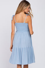 woman wearing a light blue maternity dress with adjustable tie straps and a tiered skirt, showing her back and flowing silhouette