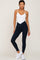 woman wearing white v-neck camisole bodysuit and navy blue crossover waistband leggings with white sneakers