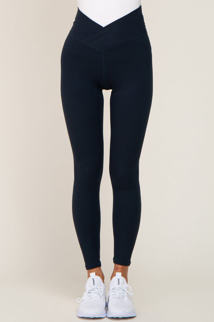 woman wearing black high-waisted leggings with a cross-front waistband and white athletic shoes