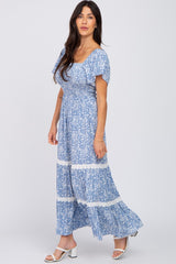 Woman wearing a blue and white floral smocked maxi dress with flutter sleeves and white lace trim