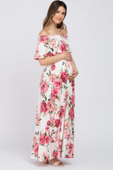 woman wearing a floral off-shoulder maternity maxi dress and cradling her baby bump