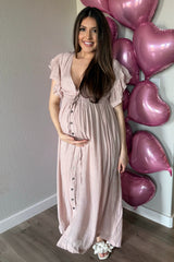 woman wearing a light pink maternity maxi dress with button details and holding her baby bump, with heart balloons in the background