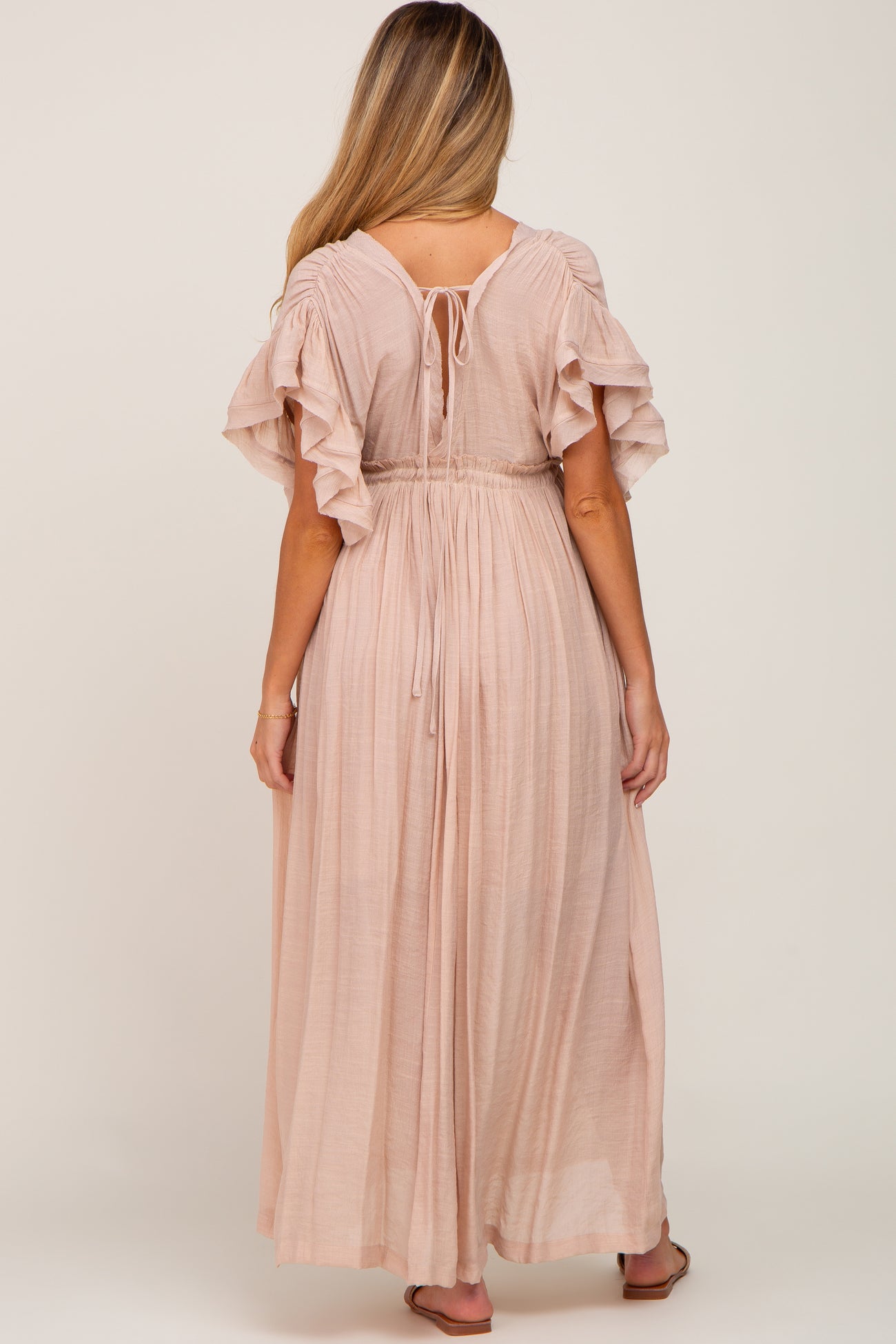 woman wearing a blush pink maternity maxi dress with ruffled sleeves and an adjustable tie back detail