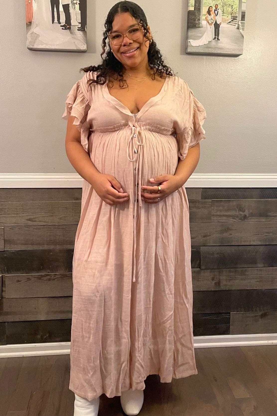 woman wearing a light pink maternity maxi dress with ruffle sleeves and a drawstring detail, showing her baby bump