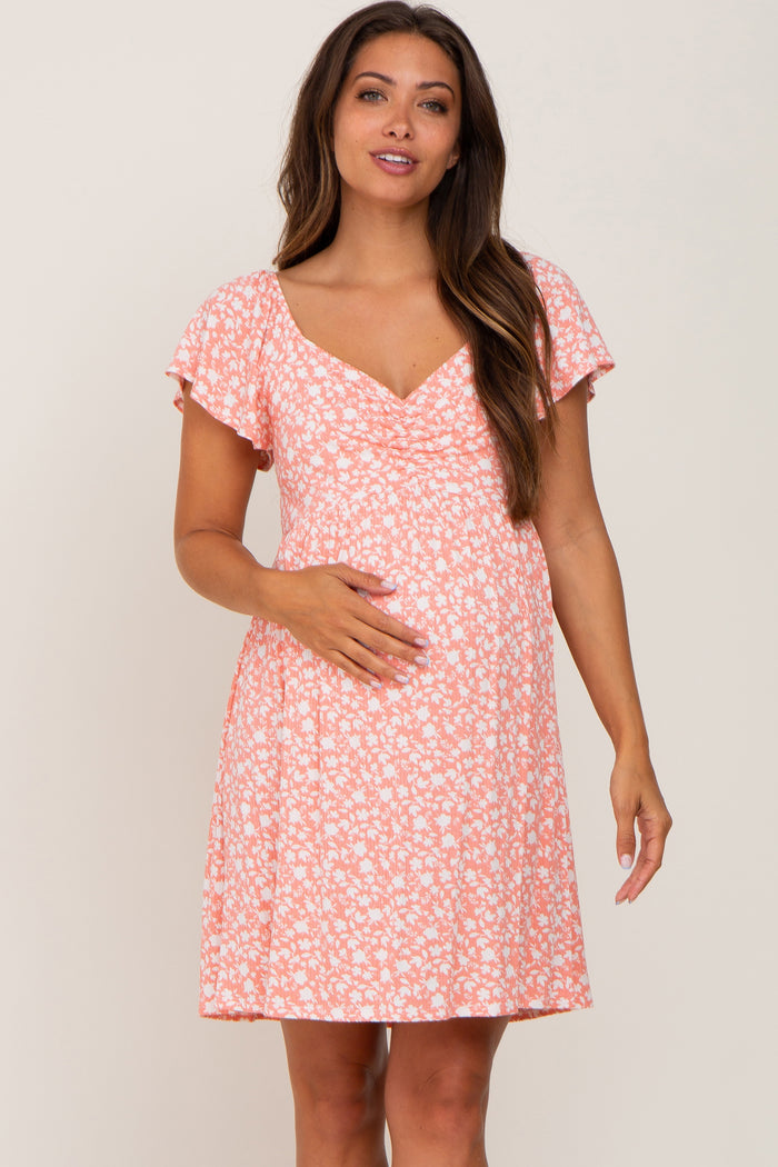 Pregnant woman wearing a peach floral print maternity dress with short flutter sleeves and a v-neckline.