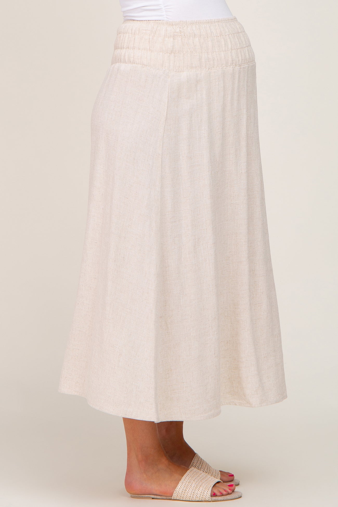 woman wearing a beige linen midi skirt with an elastic waistband and woven slide sandals
