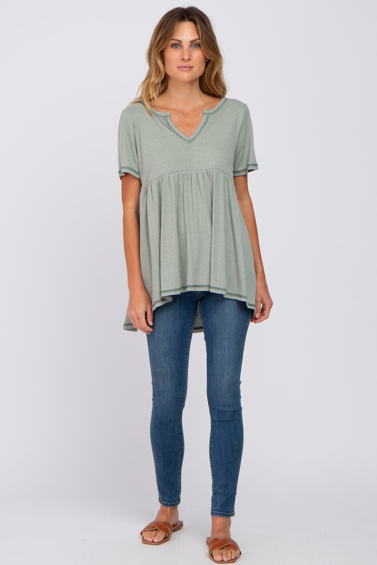 woman wearing a sage green short sleeve babydoll top and blue skinny jeans with brown sandals