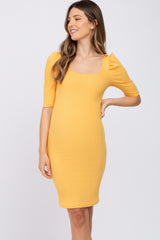 woman wearing a yellow ribbed maternity dress with puff sleeves and a fitted silhouette, highlighting her baby bump