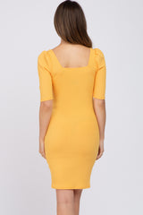 woman wearing a yellow ribbed maternity dress with short puff sleeves and a fitted silhouette