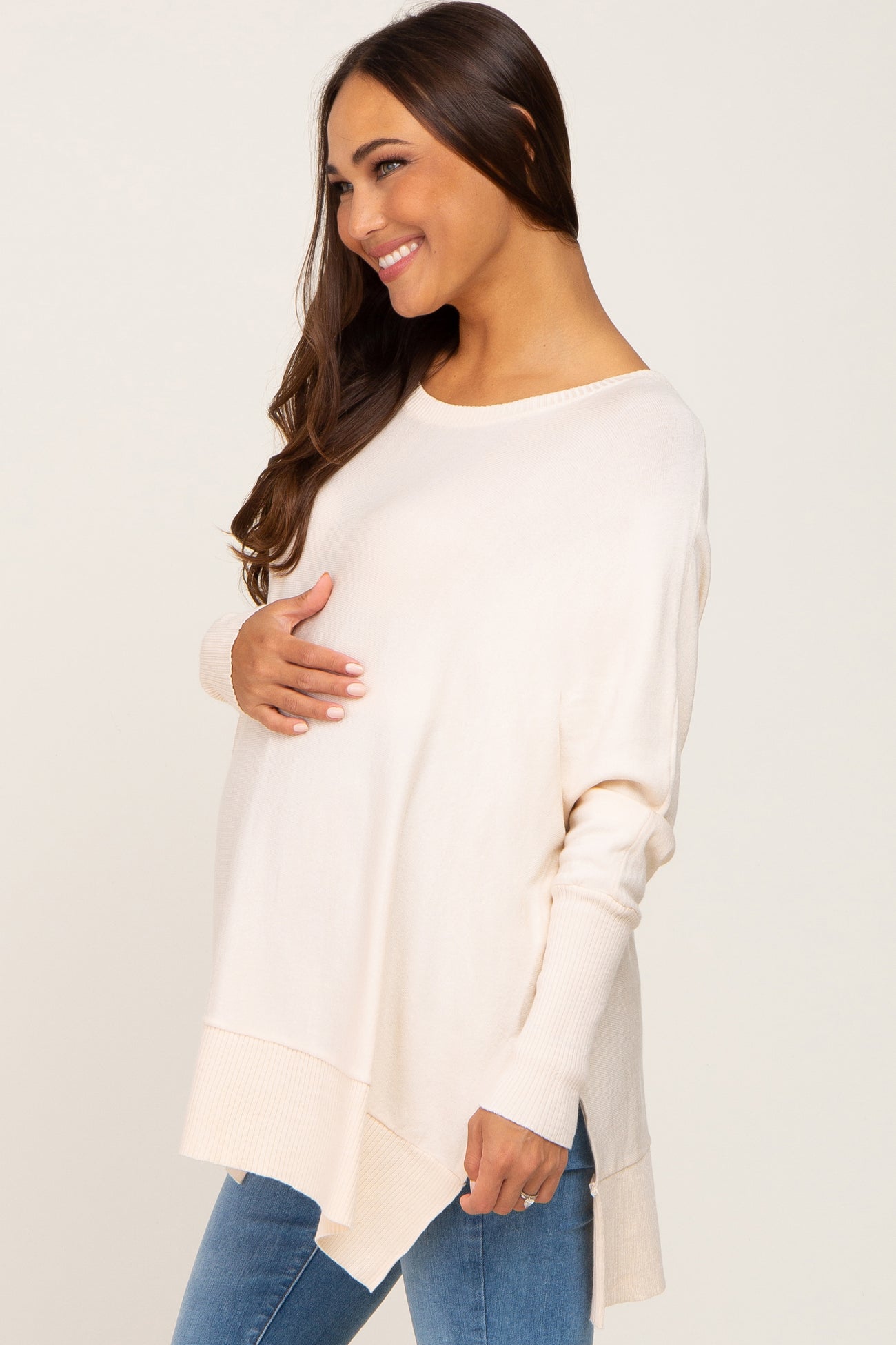 woman wearing a light beige oversized maternity sweater and gently holding her baby bump