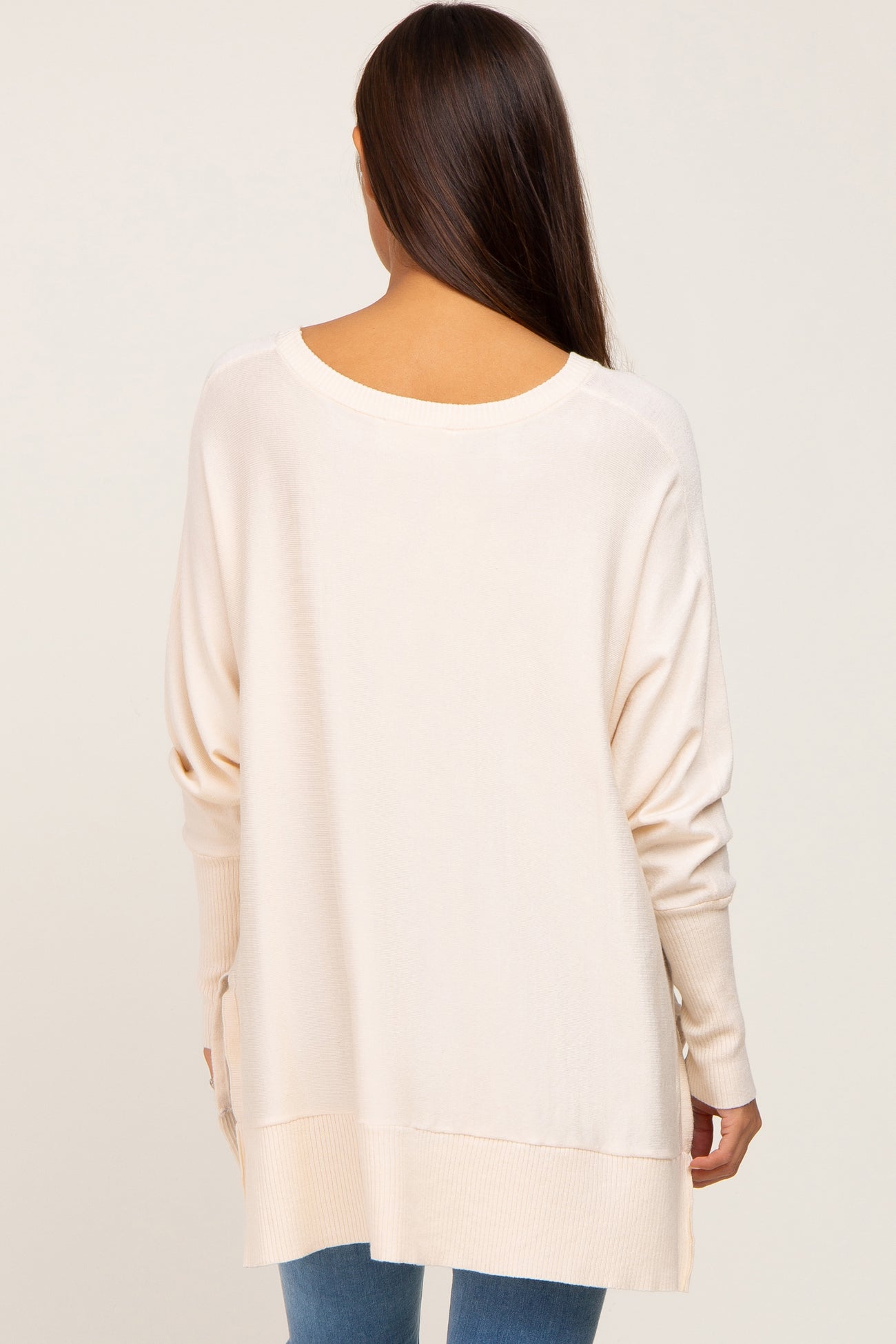 Back view of a woman wearing a cream oversized knit sweater with ribbed cuffs and hem