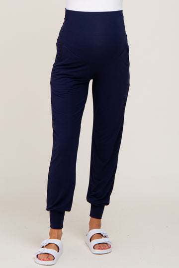 Woman wearing navy blue maternity joggers with a high waistband and white slide sandals