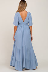 woman wearing a light blue maternity maxi dress with a smocked waist and tiered ruffles, showing a deep V-back
