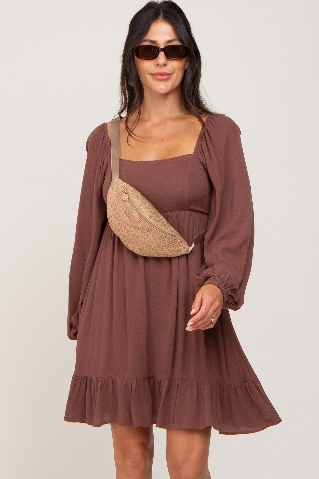 woman wearing a brown long sleeve dress with a ruffled hem and a beige crossbody bag, styled with sunglasses