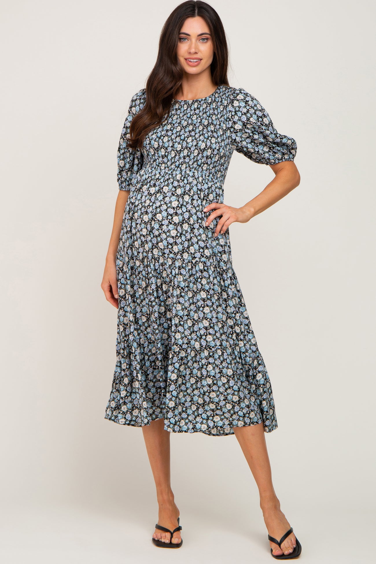 woman wearing a black floral maternity dress with puff sleeves and a flowing skirt, showcasing her baby bump