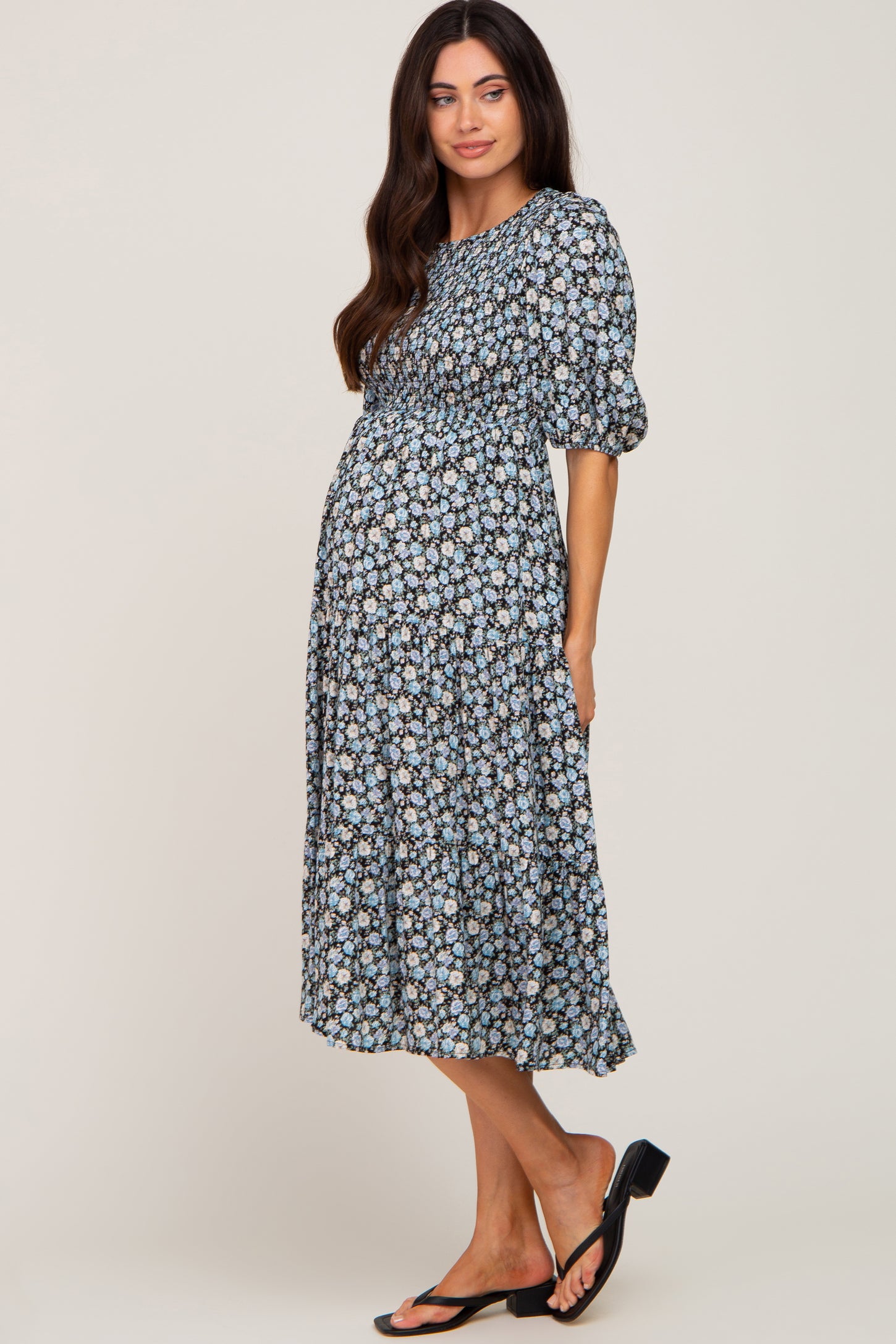woman wearing a floral maternity dress with puff sleeves and a tiered skirt, showcasing her baby bump