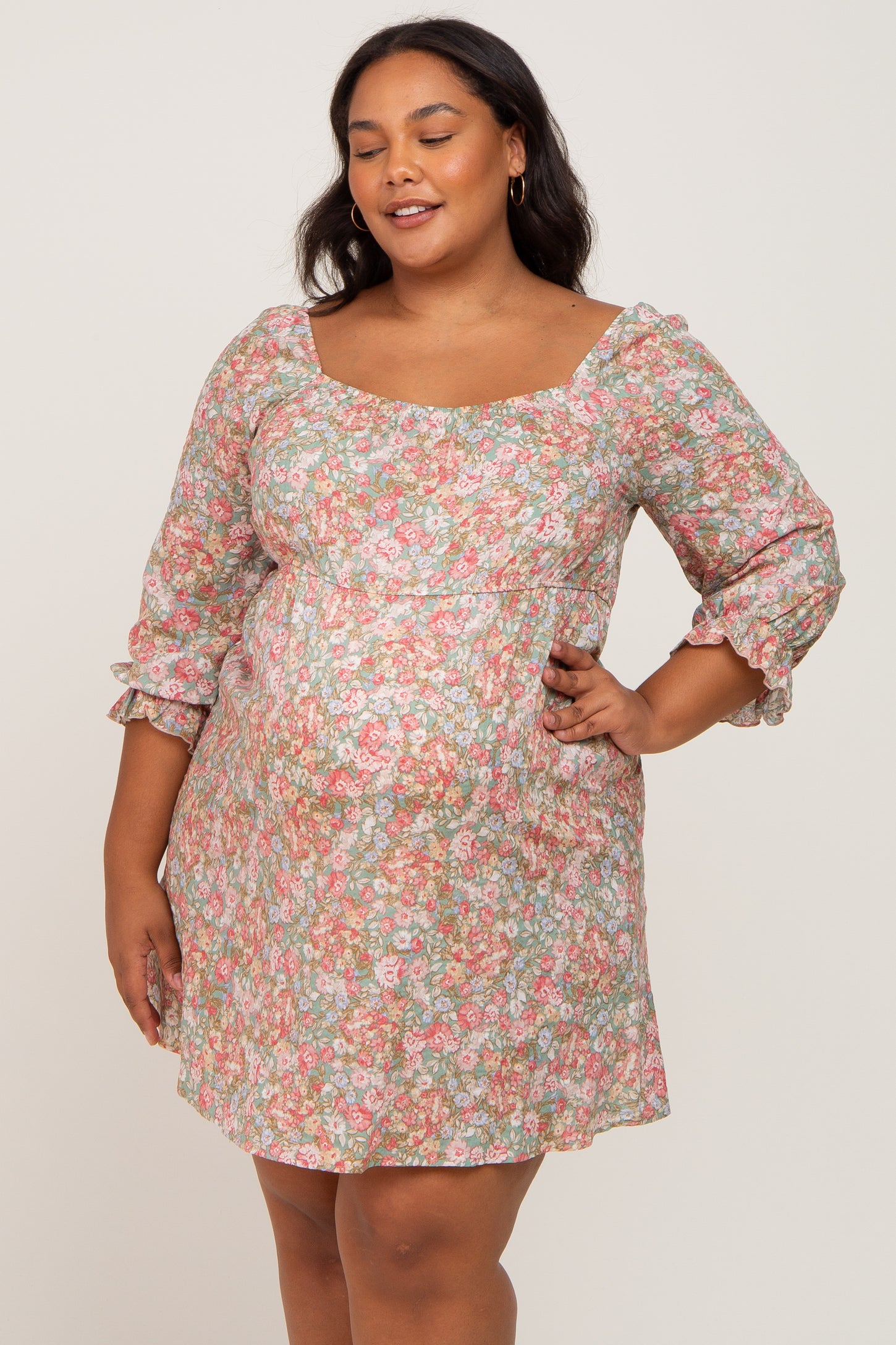 woman wearing a floral maternity plus dress with a square neckline and three-quarter sleeves, showing a baby bump