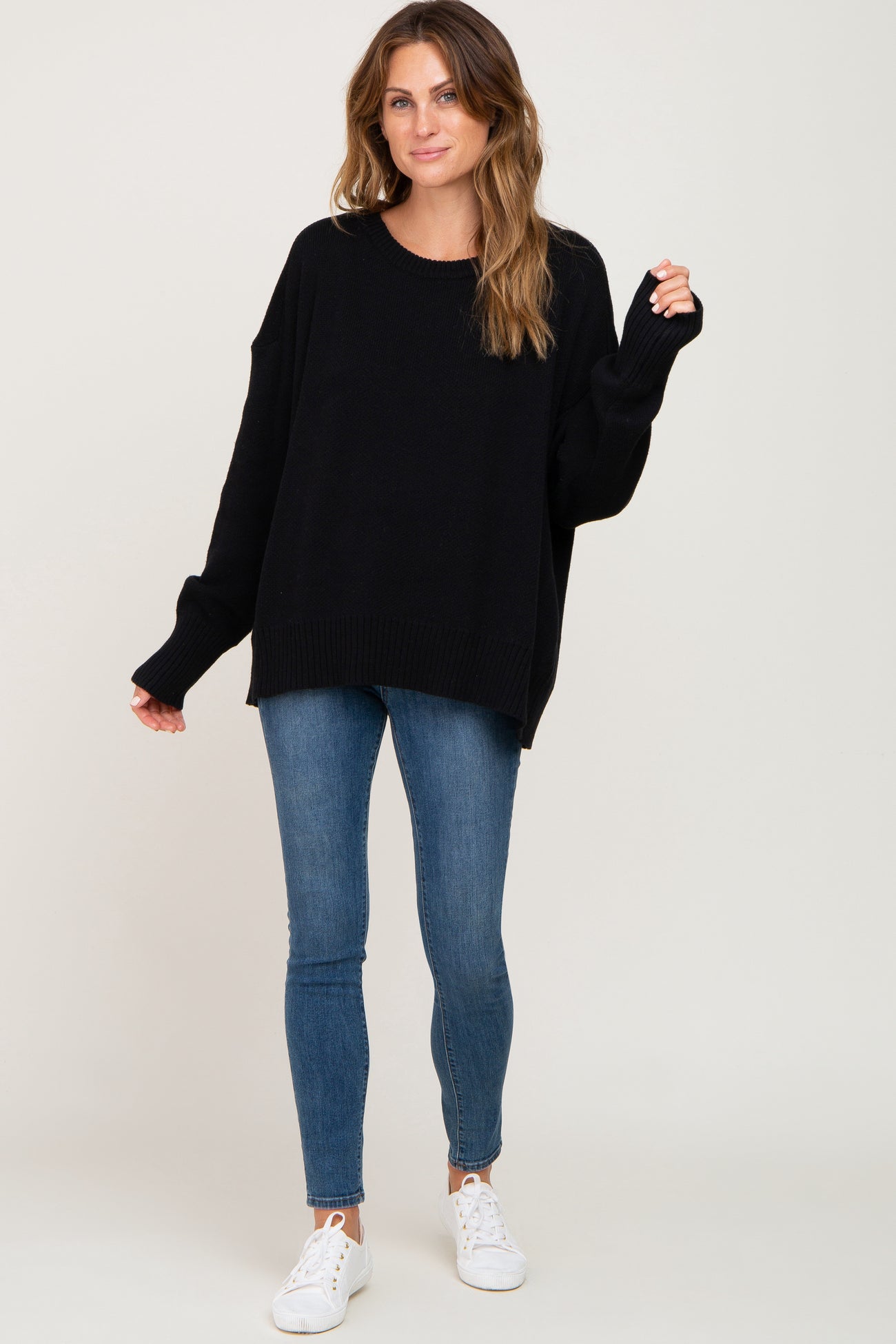 woman wearing oversized black crew neck sweater and blue skinny jeans with white sneakers