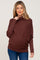 woman wearing a rust colored maternity sweater with a cowl neck and a visible baby bump