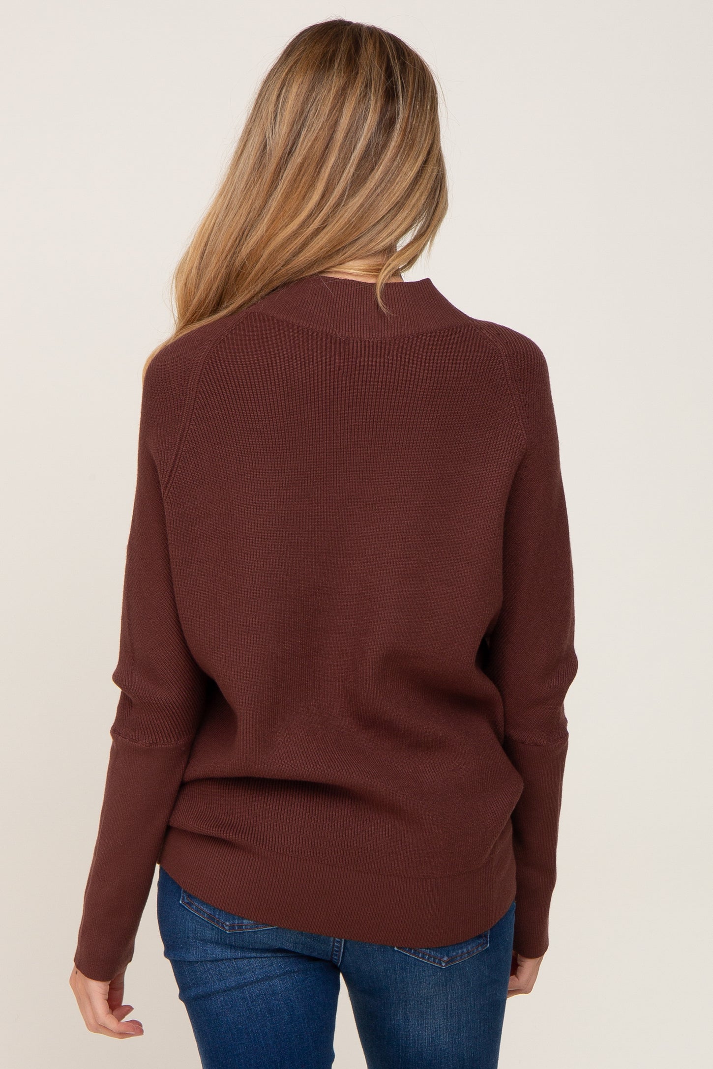 woman wearing a maroon maternity sweater, viewed from the back, styled with blue jeans