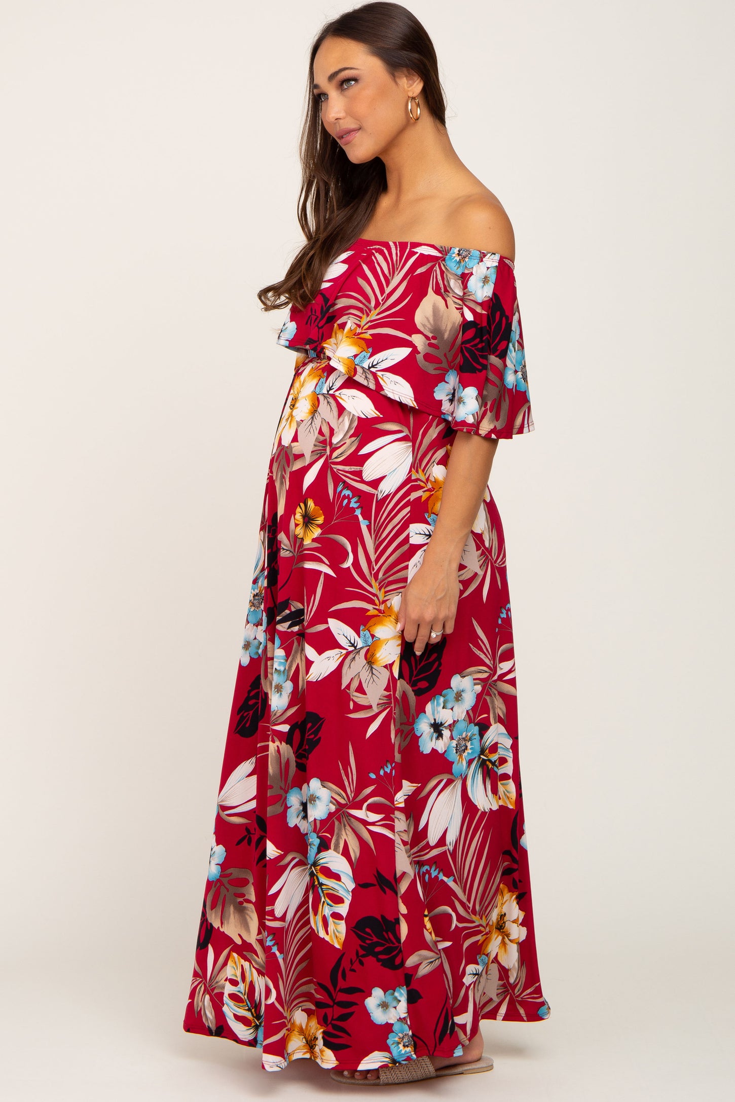 woman wearing a red floral off-the-shoulder maternity maxi dress with ruffled sleeves and a visible baby bump