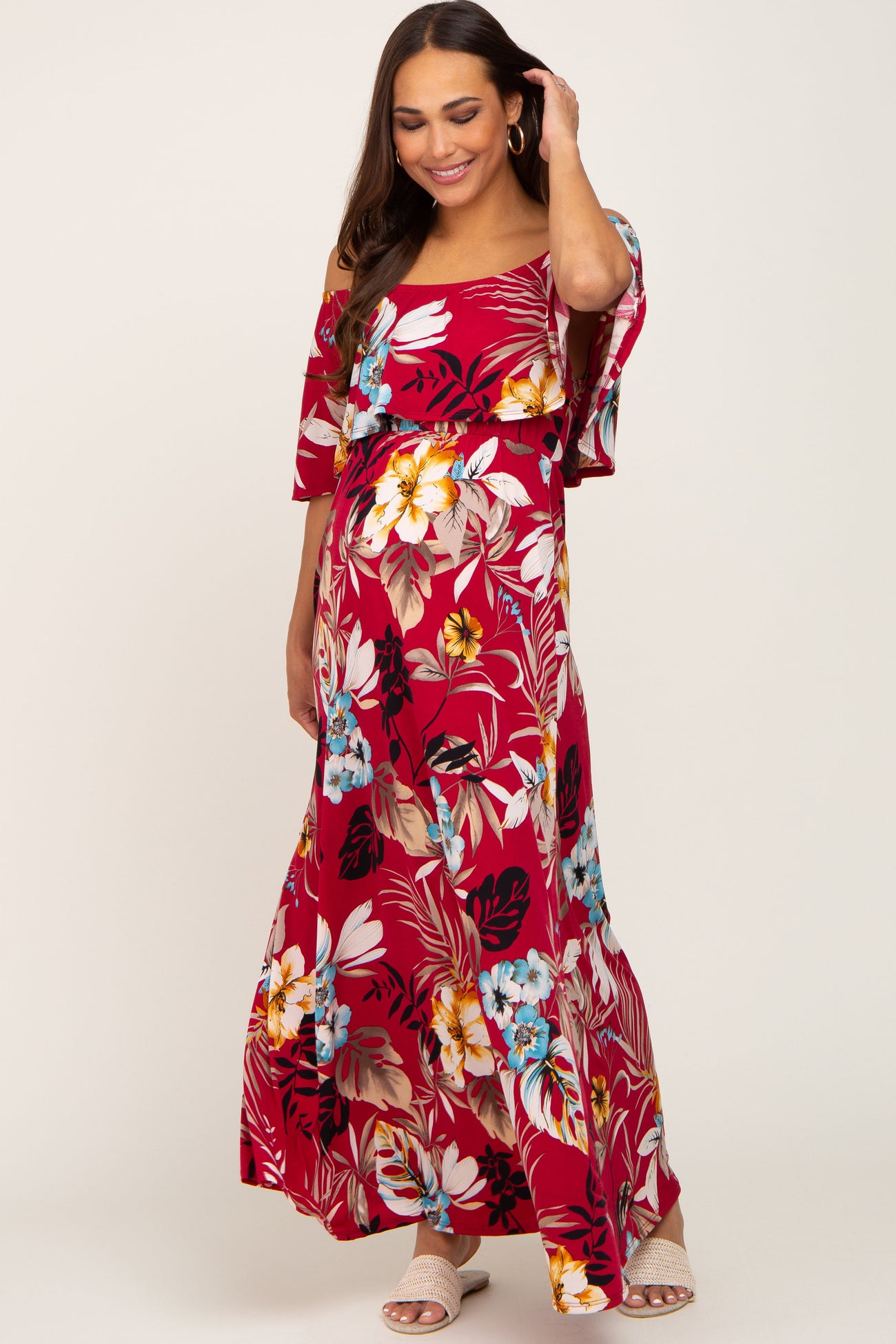 woman wearing a red floral off-shoulder maternity maxi dress with a tie waist and a visible baby bump