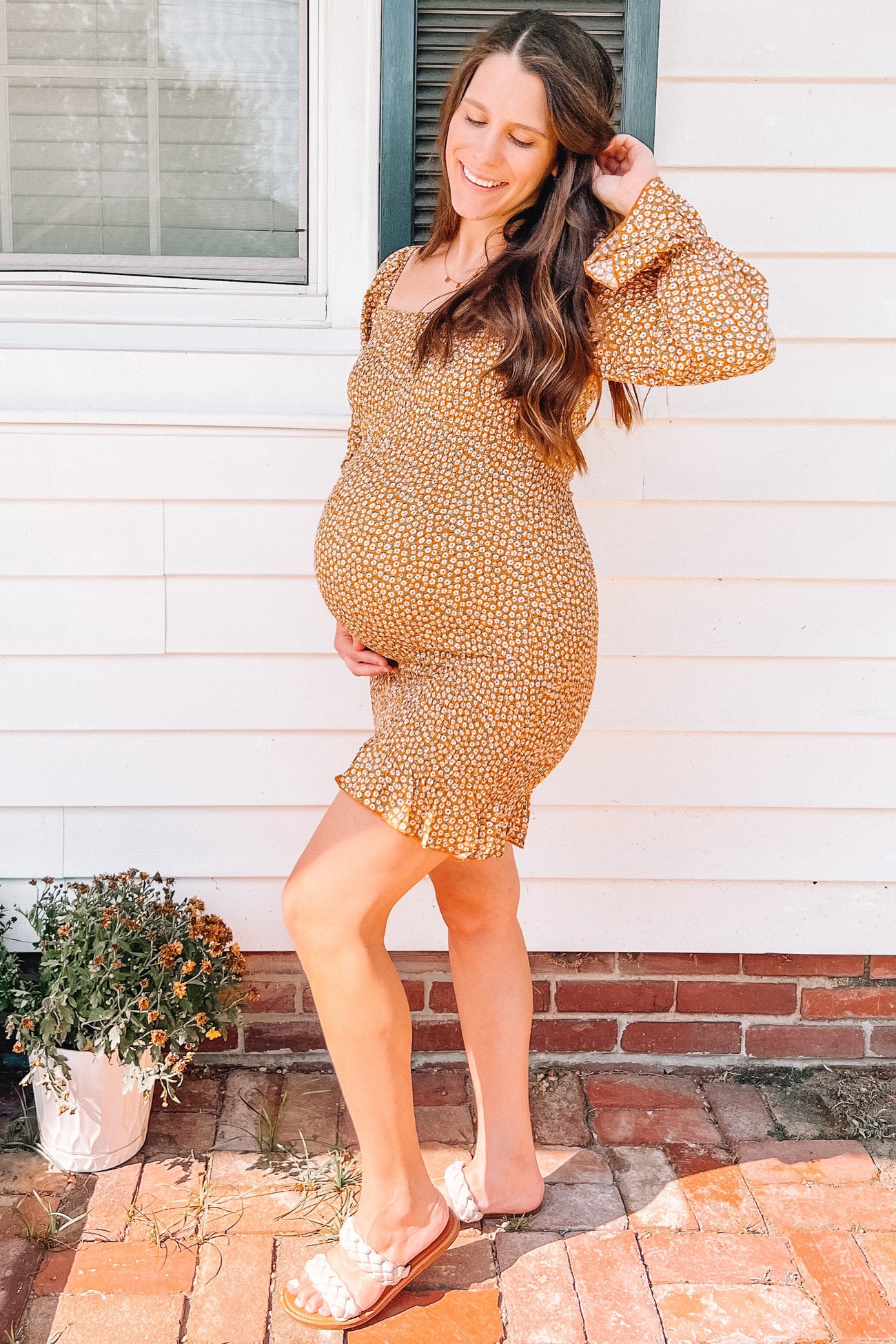 woman wearing a mustard floral maternity dress with ruffle hem and puff sleeves, showcasing her baby bump